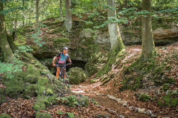 Franconian İsviçre, Bavyera, Almanya 'da kayalık bir orman patikasında elektrikli dağ bisikleti süren güzel yaşlı kadın.