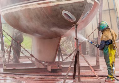 worker on a boat warf, andblasting the corroded hull of a sailing vessel clipart
