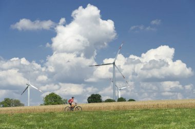 Güzel, aktif bir kadın, Almanya 'nın BadenWuerttemberg kenti Aalen yakınlarındaki Schwaebische Alb' de buğday tarlaları ve rüzgâr tekerleri arasında elektrikli dağ bisikleti sürüyor.