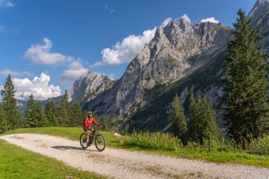 Avusturya 'nın Lechtal, Tyrol, Avusturya' nın yan vadisinde, Raintal Vadisi 'nin görkemli dağlarında elektrikli dağ bisikleti olan güzel, aktif, son sınıf öğrencisi bir kadın.