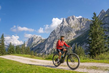Avusturya 'nın Lechtal, Tyrol, Avusturya' nın yan vadisinde, Raintal Vadisi 'nin görkemli dağlarında elektrikli dağ bisikleti olan güzel, aktif, son sınıf öğrencisi bir kadın.