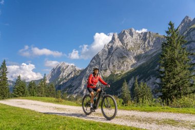 Avusturya 'nın Lechtal, Tyrol, Avusturya' nın yan vadisinde, Raintal Vadisi 'nin görkemli dağlarında elektrikli dağ bisikleti olan güzel, aktif, son sınıf öğrencisi bir kadın.