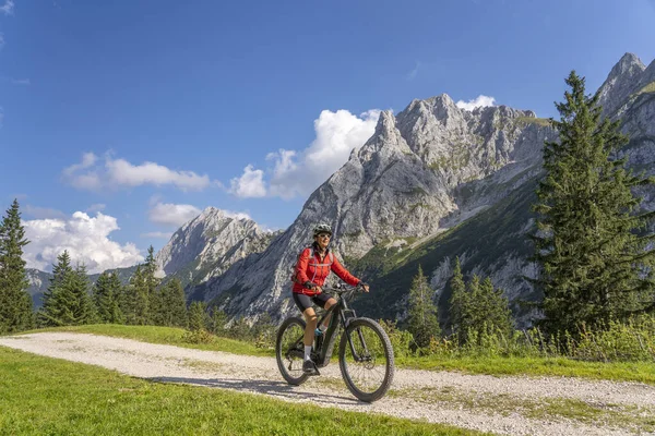 Avusturya 'nın Lechtal, Tyrol, Avusturya' nın yan vadisinde, Raintal Vadisi 'nin görkemli dağlarında elektrikli dağ bisikleti olan güzel, aktif, son sınıf öğrencisi bir kadın.