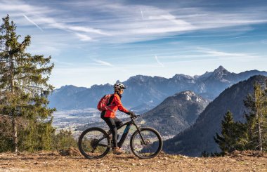 Doğu Allgaeu dağlarında elektrikli dağ bisikletine binen yaşlı güzel bir kadın. Arka planda Zugspitze Dağı, Bavyera Alpleri, Almanya
