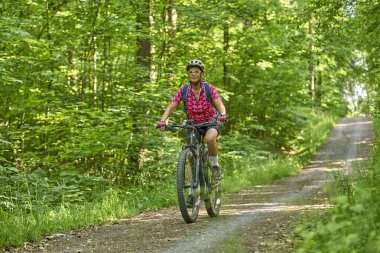 Almanya 'nın Stuttgart kentindeki yeşil şehir ormanında elektrikli dağ bisikletine binen hoş, aktif yaşlı bir kadın.