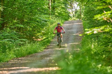 Almanya 'nın Stuttgart kentindeki yeşil şehir ormanında elektrikli dağ bisikletine binen hoş, aktif yaşlı bir kadın.