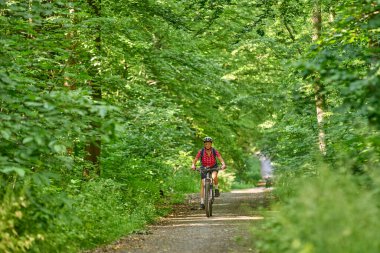 Almanya 'nın Stuttgart kentindeki yeşil şehir ormanında elektrikli dağ bisikletine binen hoş, aktif yaşlı bir kadın.