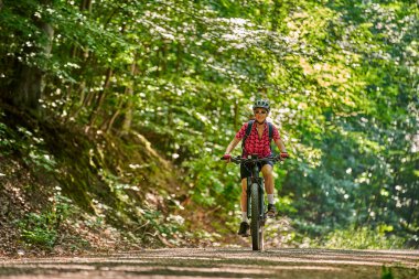 Almanya 'nın Stuttgart kentindeki yeşil şehir ormanında elektrikli dağ bisikletine binen hoş, aktif yaşlı bir kadın.