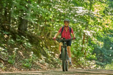 Almanya 'nın Stuttgart kentindeki yeşil şehir ormanında elektrikli dağ bisikletine binen hoş, aktif yaşlı bir kadın.
