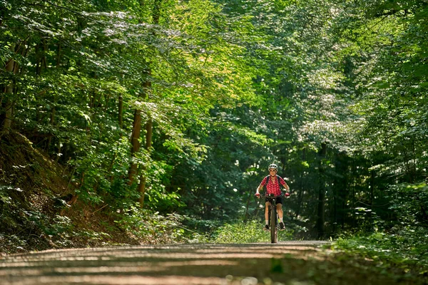 Almanya 'nın Stuttgart kentindeki yeşil şehir ormanında elektrikli dağ bisikletine binen hoş, aktif yaşlı bir kadın.