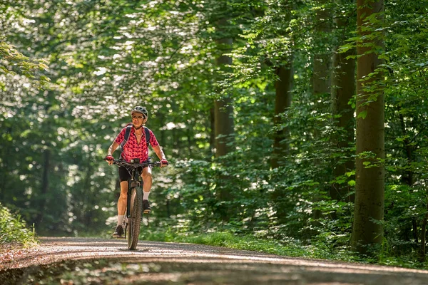 nice active senior woman riding her electric mountain bike in the green city forest of Stuttgart, Germany