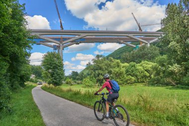 Stuttgart 'tan Münih' e giden yeni tren yolu için inşaat alanının altında elektrikli dağ bisikletli bir kadın. Fils Valley, Bden-Wrttemberg, Almanya 'da birleşik tünel ve köprü inşaatı 