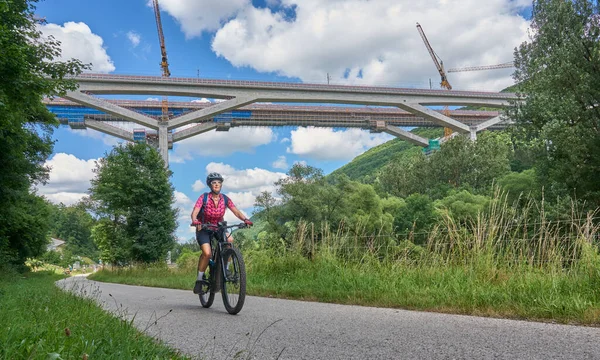 woman on electric mountain bike below the construction site for the new railway trail from Stuttgart to Munich. Combined tunnel and bridge construction in the Fils Valley, Bden-Wrttemberg, Germany