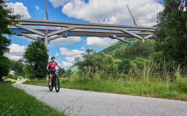 woman on electric mountain bike below the construction site for the new railway trail from Stuttgart to Munich. Combined tunnel and bridge construction in the Fils Valley, Bden-Wrttemberg, Germany