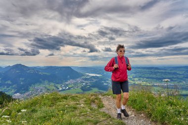 nice senior woman hiking at Mount Gruenten in the Allgaeu Alps with awesomw view over Iller valley to Lake Alpsee and Lake of Constanz, Bodensee, Bavaria, Germany
