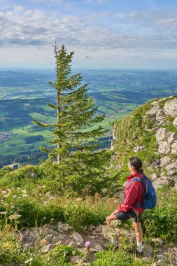 nice senior woman hiking at Mount Gruenten in the Allgaeu Alps with awesomw view over Iller valley and the Allgaeu low lands, Bavaria, Germany