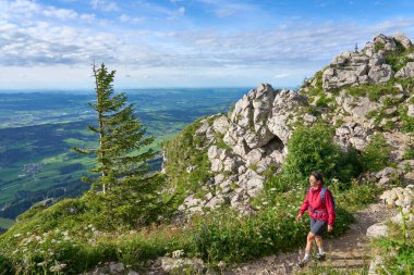 nice senior woman hiking at Mount Gruenten in the Allgaeu Alps with awesomw view over Iller valley and the Allgaeu low lands, Bavaria, Germany