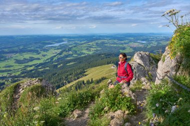nice senior woman hiking at Mount Gruenten in the Allgaeu Alps with awesomw view over Iller valley and the Allgaeu low lands, Bavaria, Germany