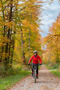 pretty senior woman on electric bicycle in a colorful autumn forest with golden foliage in Baden-Wuerttemberg, Germany