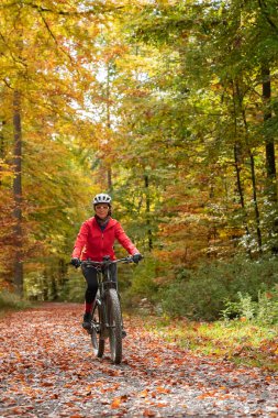 pretty senior woman on electric bicycle in a colorful autumn forest with golden foliage in Baden-Wuerttemberg, Germany