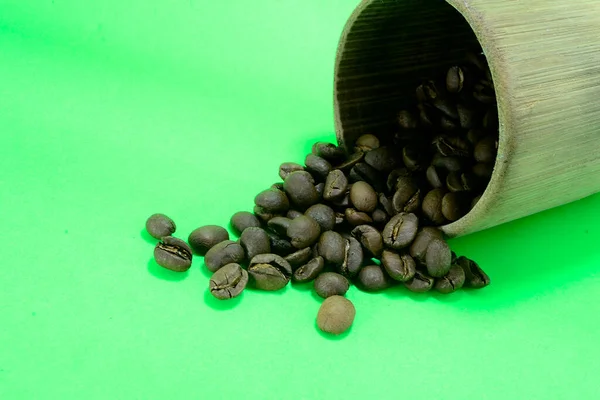 Bambu bardağındaki kahve çekirdekleri dağınık. Fotoğraf yeşil arkaplanda