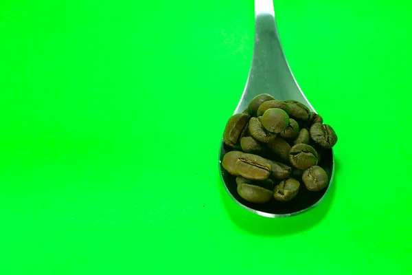 Yeşil Arka Planda Kaşık Üzerinde Kahve Çekirdekleri — Stok fotoğraf