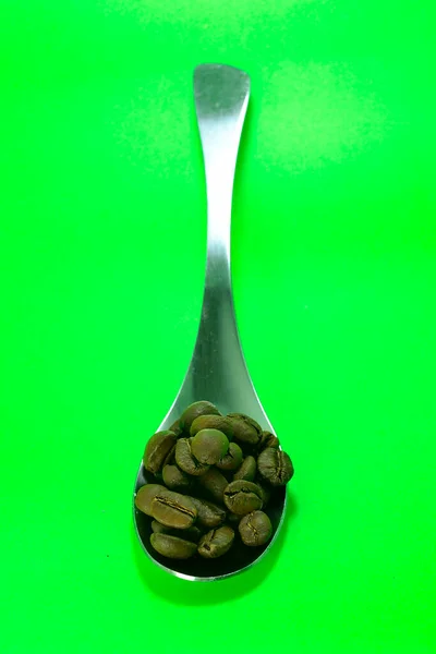 Yeşil Arka Planda Kaşık Üzerinde Kahve Çekirdekleri — Stok fotoğraf