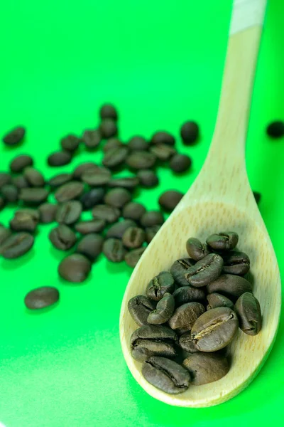 Coffee beans on a bamboo spoon. There is coffee scattered with a green background