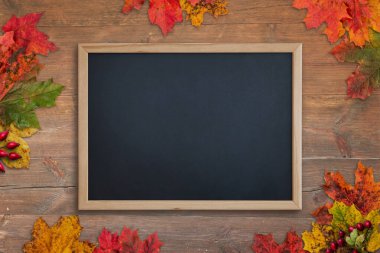Sonbahar yapraklarıyla çevrili ahşap masanın üzerinde temiz bir karatahta. Üst görünüm, düz konum