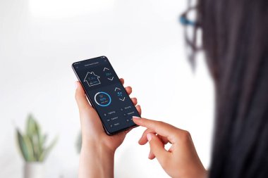 Akıllı ev uygulaması konsepti, akıllı telefondan kadınların eline geçiyor. Arka planda ev içi