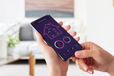 Akıllı telefon kavramı üzerine modern akıllı ev kontrol uygulaması. Akıllı telefon ve kontrole sahip kadın sıcaklık, ışık, müzik ve güvenlik sistemi