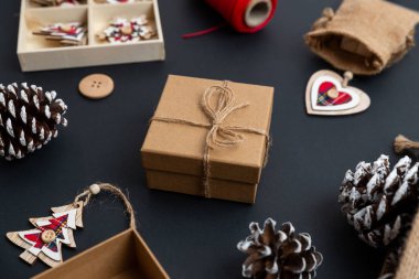 Noel hediyesi. Masasında sicim fiyonk var. Noel süsleriyle çevrili. Çam kozalakları, ahşap süslemeler, kırmızı iplik, masada çuval. Yakın plan.