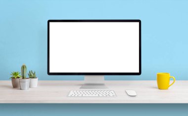 Çalışma masasında sunum için beyaz izole ekran ile bilgisayar görüntüsü. Kahve fincanı ve bitkilerle temiz kompozisyon. Arkaplanda mavi duvar