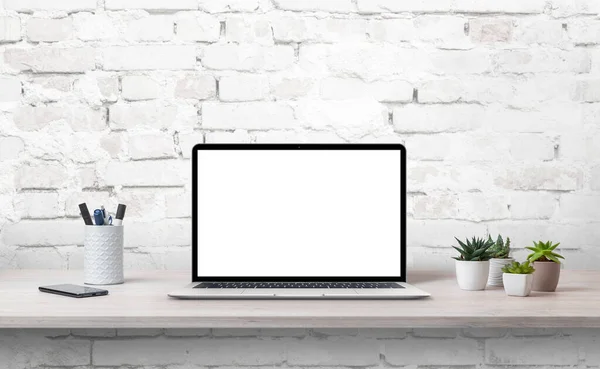 写字台上的笔记本电脑 装有等高屏幕 可模拟 旁边的植物 电话和钢笔 背景为白砖墙 — 图库照片