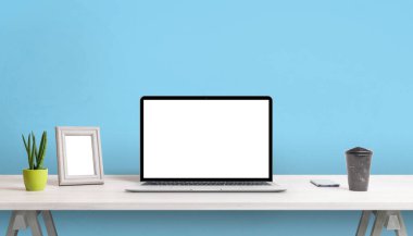Çalışma masasında boş ekranı olan bir laptop. Resim çerçevesi, bitki, kahve ve telefon. Arkaplanda mavi duvar