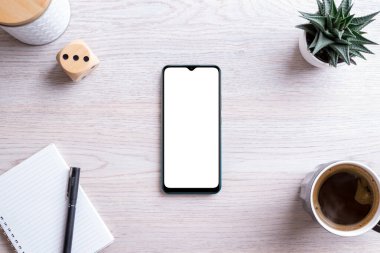 Çalışma masasının üzerinde düz telefon modeli kompozisyonu vardı. Uygulama sunumu için izole ekran. Kalemli ped, kahve fincanı, bitki ve kutu yanında. Temiz ofis masası