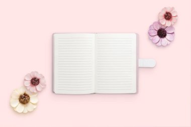Pembe yüzeydeki çiçeklerle çevrili bir not defteri. Mesaj için boş kağıtlar. Düz konum, üst görünüm bileşimi