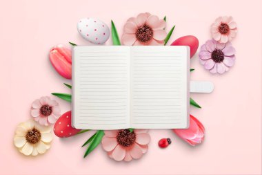 Paskalya süsleriyle çevrili bir defter. Tebrik mesajı için boş kağıt. Üst manzara, düz uzanma