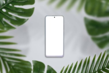 Gri yüzeyde yeşil yapraklarla çevrili bir telefon modeli. Üst görünüm, düz konum