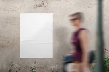 Tasarım sunumu için duvarda boş poster modeli var. Genç bir kadın geçiyor.