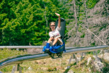Girl rides a mountain roller coaster and waves. Mountain environment with trees in the background