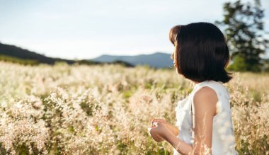Asian girl in white dress in field at sunset, outdoors enjoying nature concept.