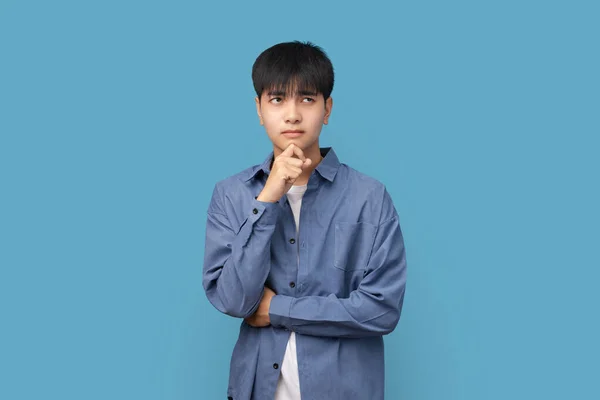 若いハンサムなアジアの男の肖像画は思考を考え 青い背景に立ってコピースペースと横に見て 何かを考える — ストック写真