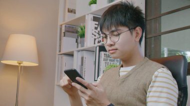 Oturma odasında akıllı telefon kullanan genç bir adam..
