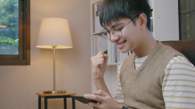 Genç çocuk kazanmaktan mutlu. Oturma odasındaki akıllı telefondan oyun oynuyor..