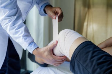 Doktor danışman hastanın dizine sargı bezi sarmış. Yaraları iyileştir.
