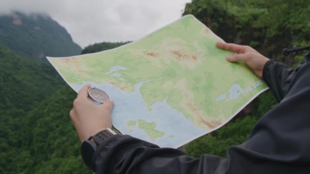 キャンプのためのハイキング中に山の頂上で位置と方向を確認して検索するための旅行者の手の中のコンパスと地図 — ストック動画