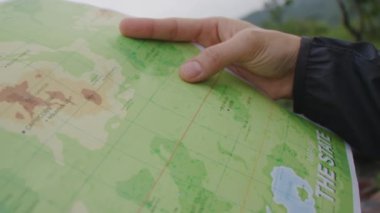 Compass and map in hands of traveler for checking and searching position and direction at the top of peak of mountain while hiking for camping