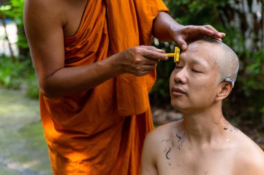 Asian man shaving his head by elder monk before ordain ceremony, Study the Dharma according to the teachings of the Buddha.