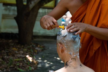Asian man shaving his head by elder monk before ordain ceremony, Study the Dharma according to the teachings of the Buddha.